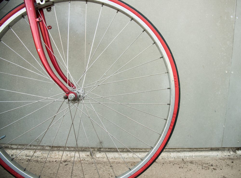 Bicycle wheel stands still against a concrete wall, showcasing a red frame and rim.