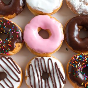 A variety of donuts are arranged in a box, featuring diverse toppings like sprinkles, chocolate, and pink icing, creating a vibrant assortment.