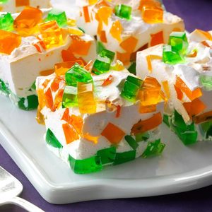 Colorful gelatin squares embedded in creamy dessert, resting on a white rectangular plate, creating a vibrant, inviting display.