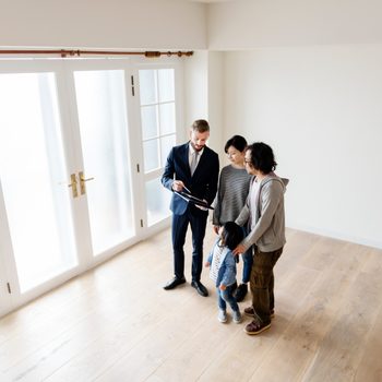 Agent shows paperwork to family in empty room with wooden floor and large frosted glass doors.