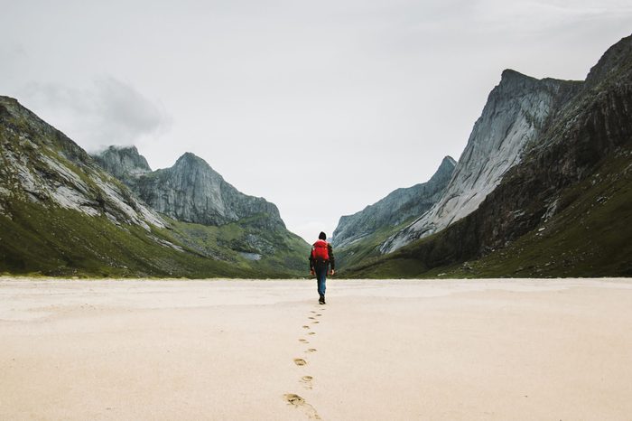 Man with backpack walking away alone at sandy beach in mountains Travel lifestyle concept adventure outdoor summer vacations in Norway wild nature