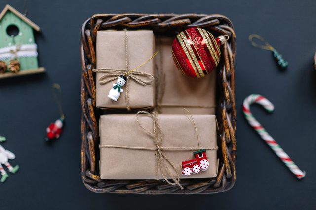 Wicker basket holds wrapped gifts and a red ornament; set against a dark background with candy cane and small holiday decorations nearby.