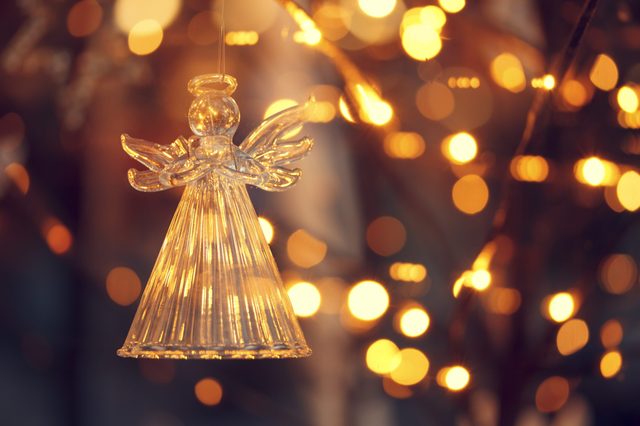 Glass angel ornament hanging amid blurred warm lights, creating a festive, glowing atmosphere.