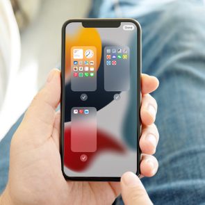 A hand holds a smartphone displaying app folders, with faded check marks, in a comfortable setting of jeans and soft focus background.