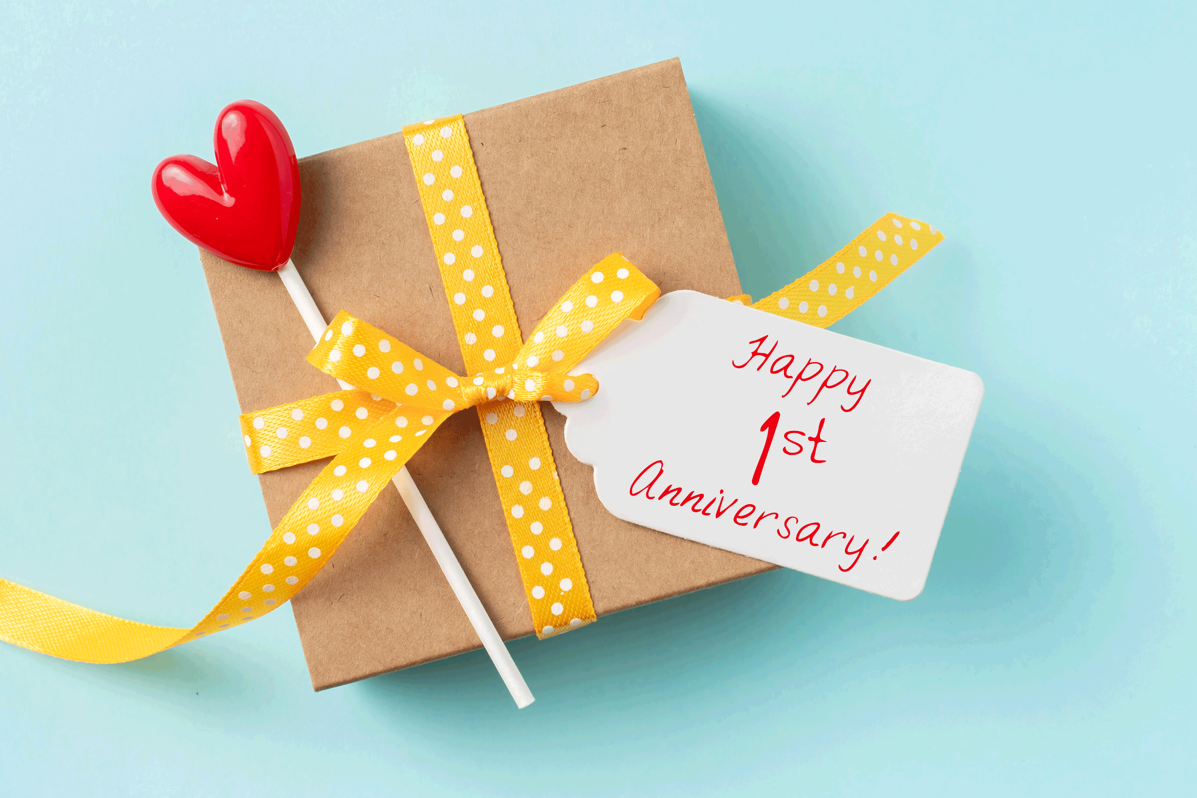 Gift box tied with yellow polka dot ribbon, heart-shaped lollipop beside, 