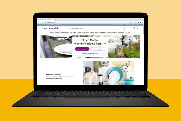 Laptop displays Wayfair wedding registry webpage; features buttons for creating or finding a registry amidst wedding decorations and gifts on a yellow surface.