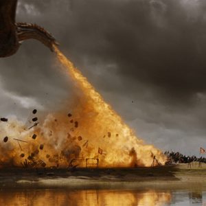 Dragon breathes fire, causing explosion, amidst medieval battlefield with soldiers and weapons under stormy skies near a reflective body of water.