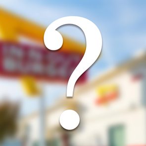 A large white question mark overlays a blurry background depicting a fast-food restaurant sign and building under a blue sky.