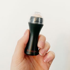 Hand holding a black Revlon makeup applicator with a clear cap, set against a plain white background.
