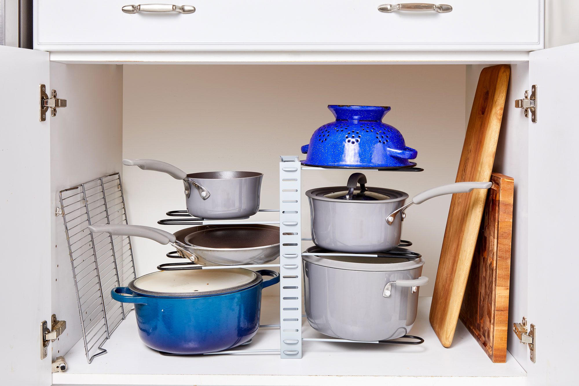 Cookware is neatly organized on a kitchen shelf, featuring pots, pans, and a blue colander, with cutting boards and a cooling rack nearby.
