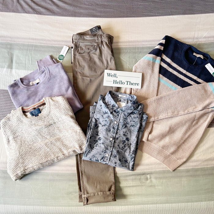 Clothes are neatly arranged on a striped bedspread. Includes sweaters, pants, and a patterned shirt. A card reads, â€œWell, Hello There.â€
