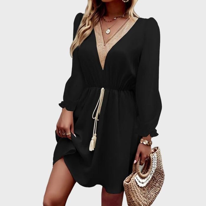 A person wears a black dress with gold trim, holding a woven handbag, against a plain white background.