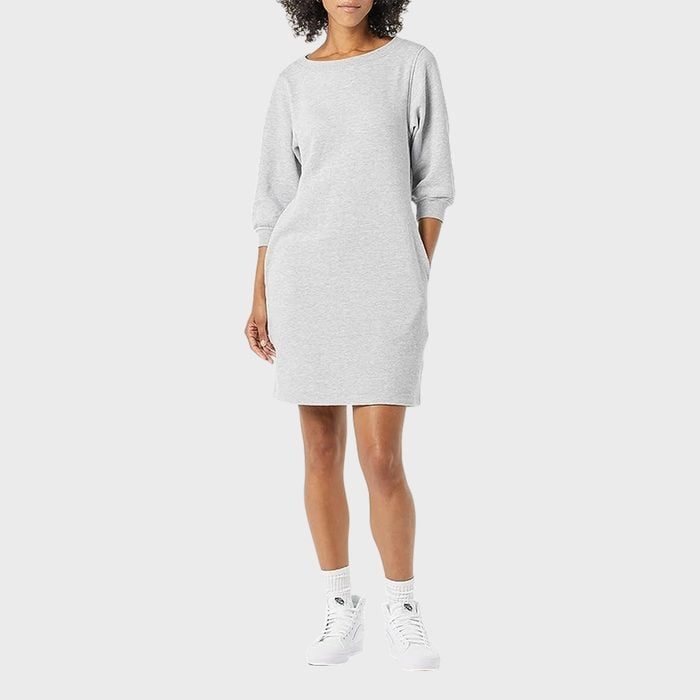A person wearing a casual gray dress and white sneakers stands against a plain background.