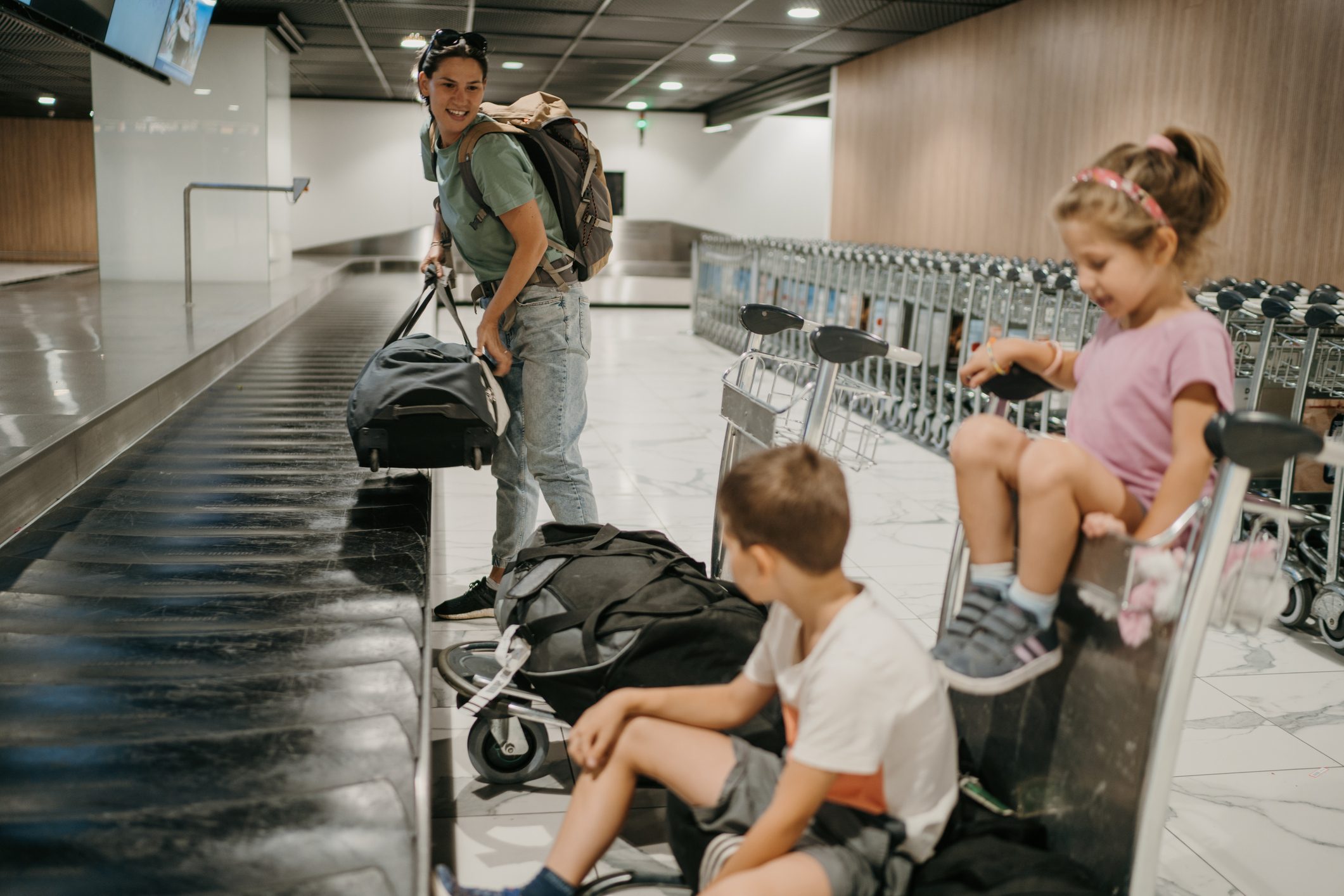 Family collecting luggage at belt conveyor with carts against the belt